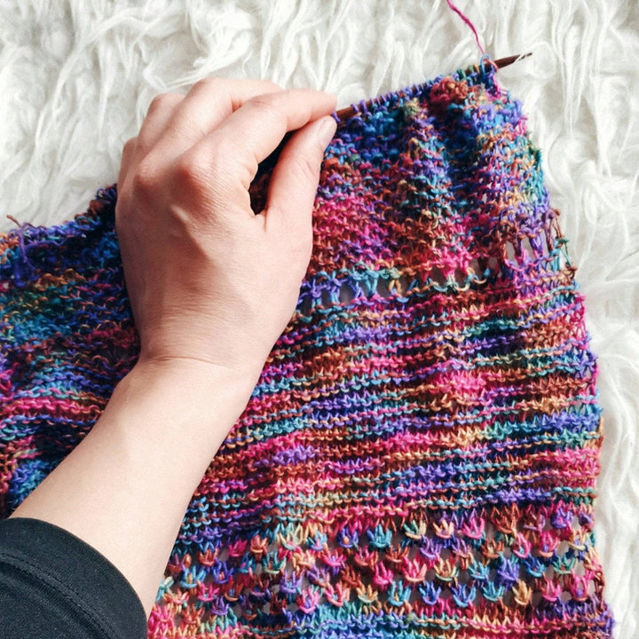 in progress pink, purple , blue, brown knit shawl on a white background