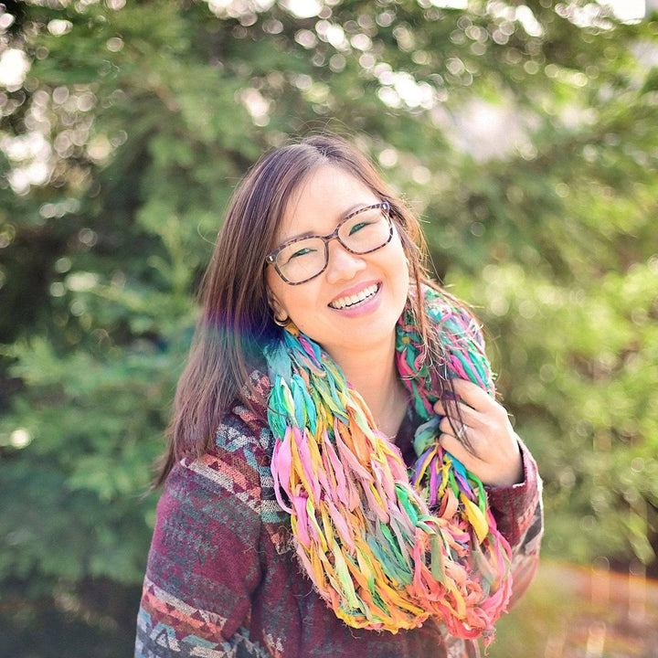 girl smiling wearing a multicolored scarf with trees in the background