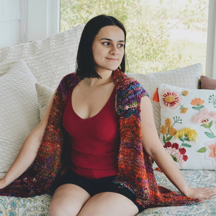 A woman sitting on the couch wearing yarn crochet vest.