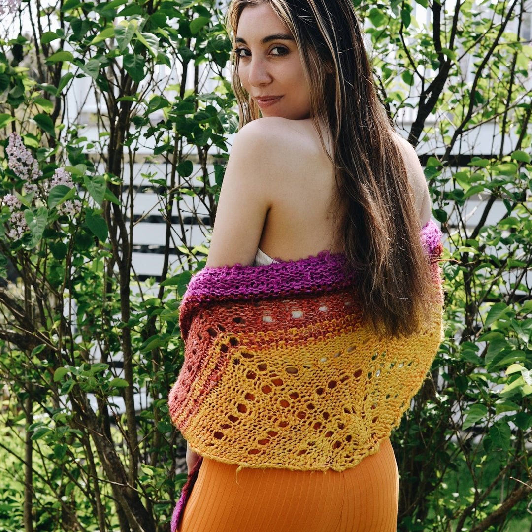 Lifestyle picture of a woman wearing a colorful shawl made from Plant Based Banana Fiber Yarn. The shawl, draped elegantly over her shoulders, features vibrant shades of purple, orange, and yellow, highlighting the unique texture and soft quality of the handspun banana fibers. This eco-friendly accessory adds a touch of exotic elegance to her outfit.