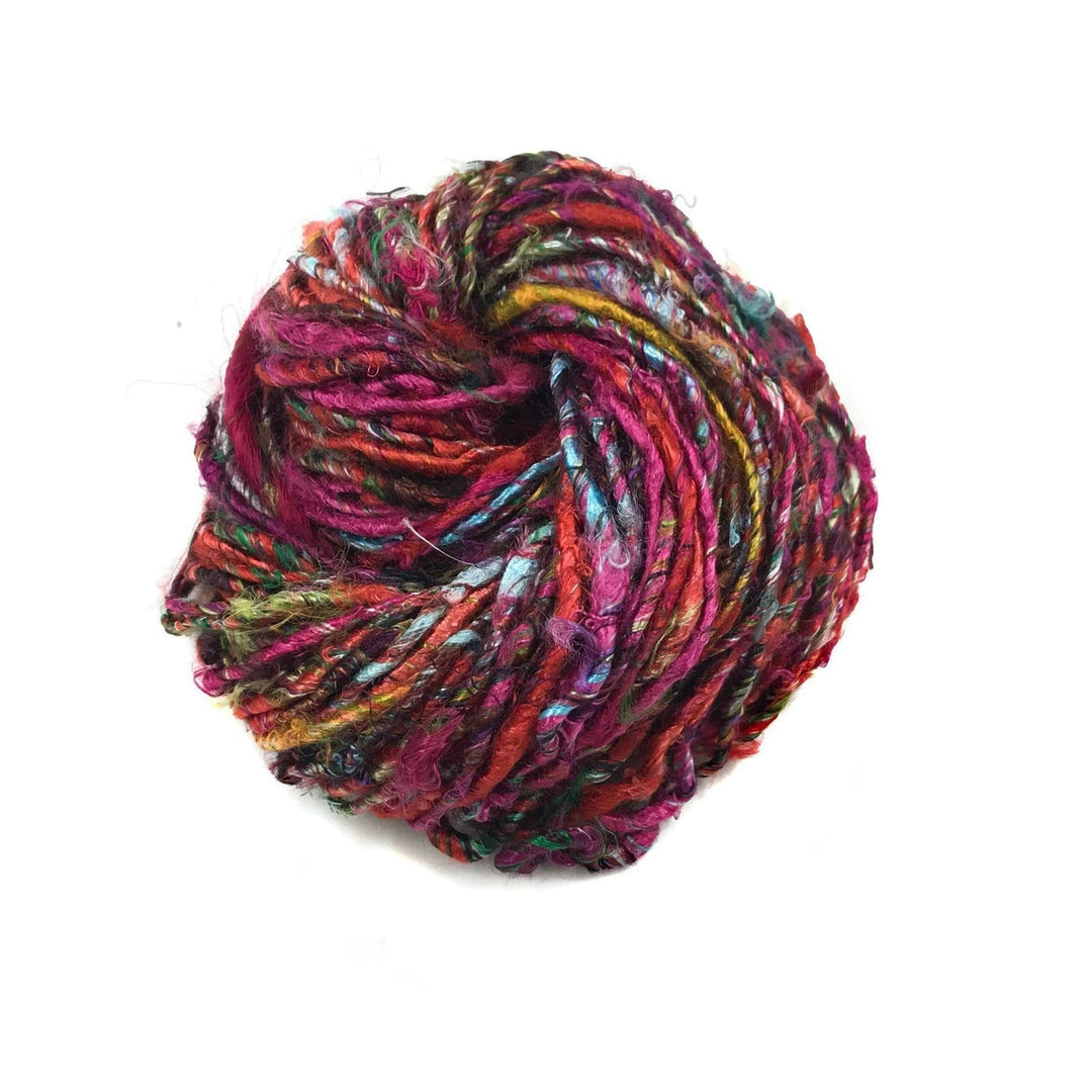 Close-up image of a skein of Plant Based Banana Fiber Yarn in a rich blend of red and multicolored fibers. The handspun yarn features a soft and vibrant texture, ideal for eco-friendly knitting and crocheting projects.