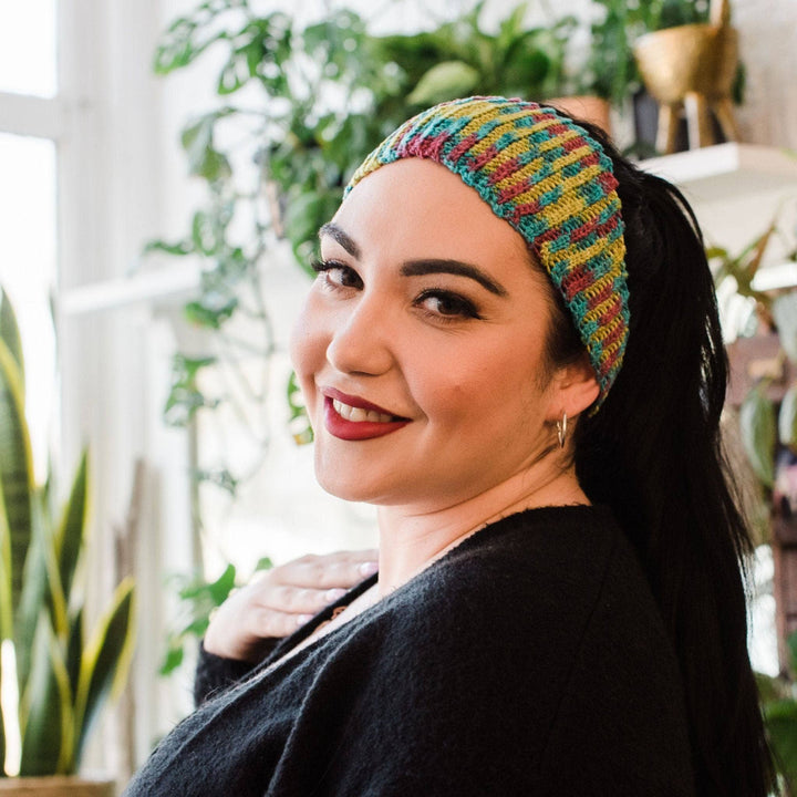 Model wearing plume headband (out of stock colorway) with potted greenery in the background.