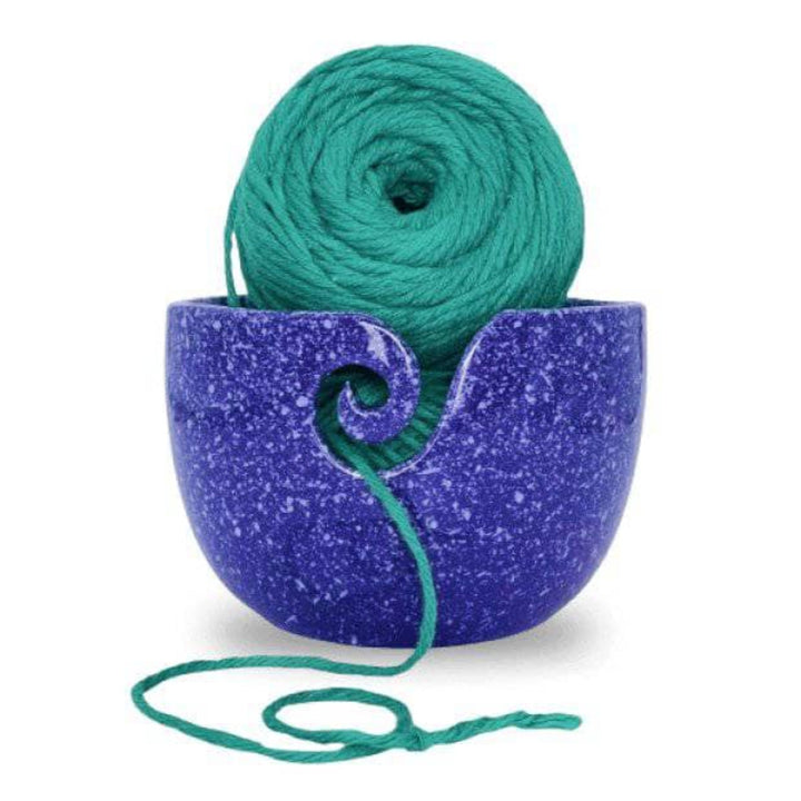 Purple Cosmic Ceramic Yarn Bowl with white speckles, holding a ball of green yarn, displayed against a white background. This celestial-themed yarn bowl helps keep yarn clean, organized, and untangled during knitting or crochet projects.