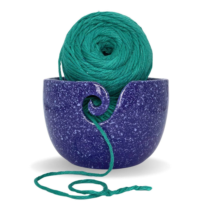 Purple Cosmic Ceramic Yarn Bowl with white speckles, holding a ball of green yarn, displayed against a white background. This celestial-themed yarn bowl helps keep yarn clean, organized, and untangled during knitting or crochet projects.