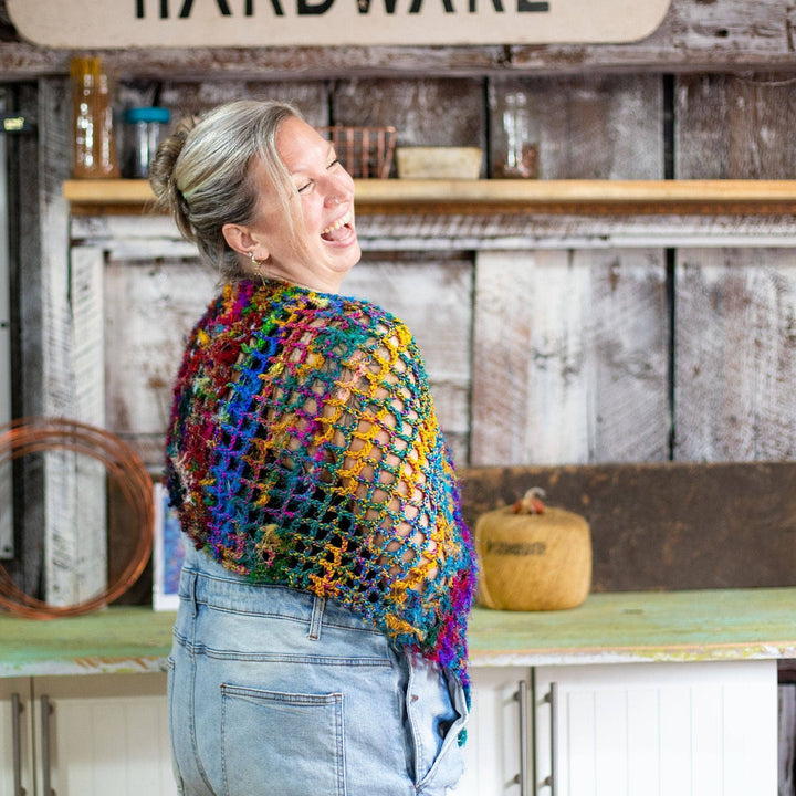 model wearing quadramesh shawl facing 3/4 away from the camera laughing in front of a barn wall background.