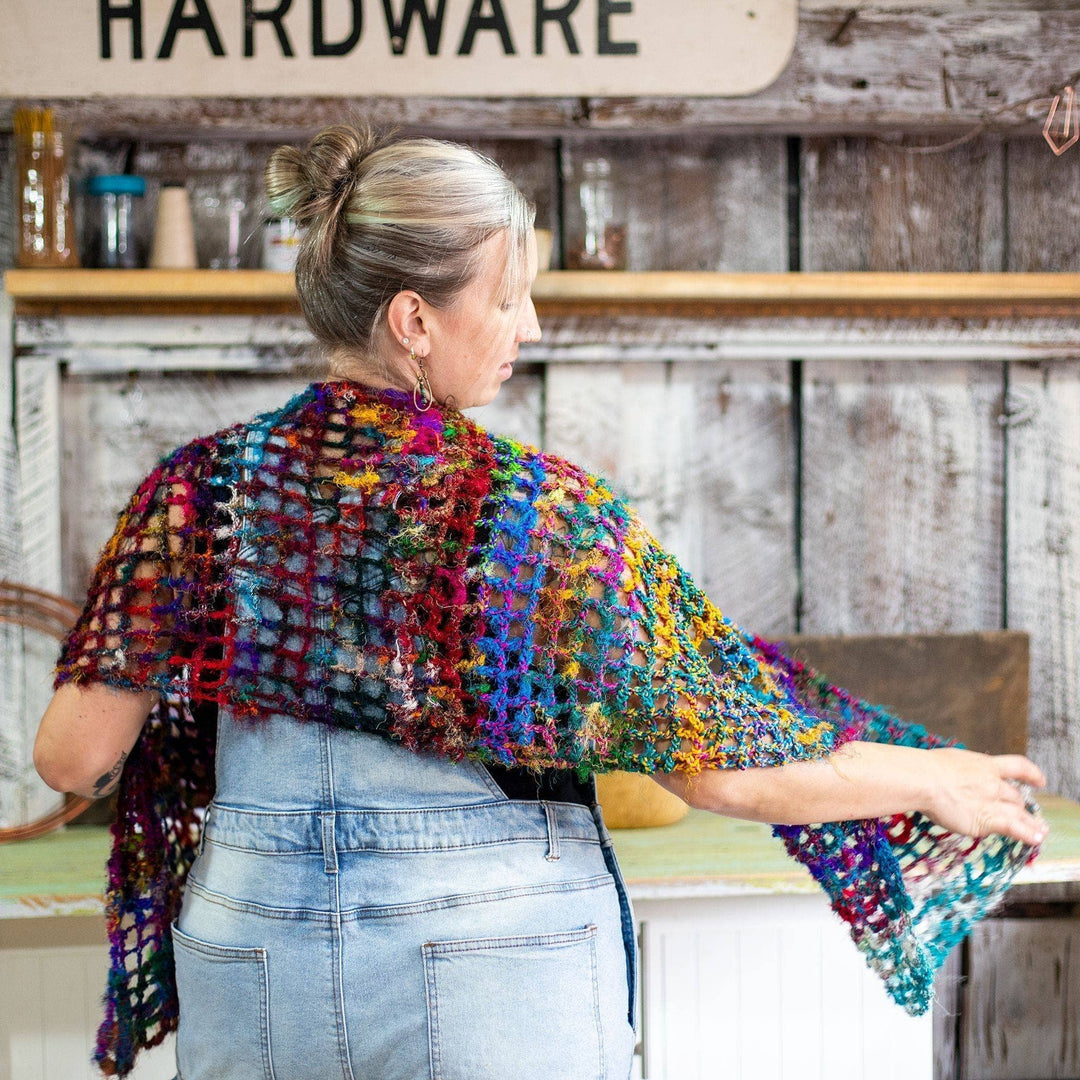 Model facing away from the camera wearing quadramesh shawl with a barn wall in the background.