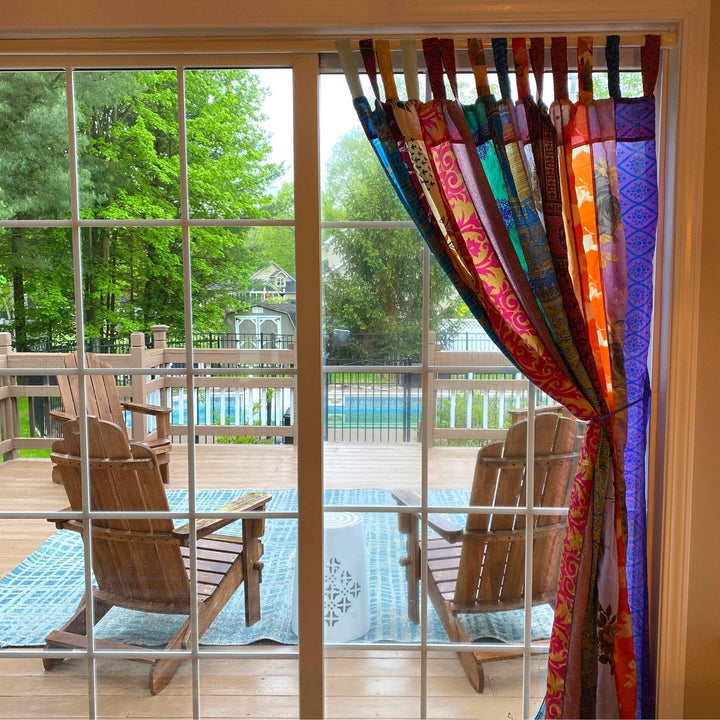 Sari silk curtains hanging above a patio door with the view of outside. 