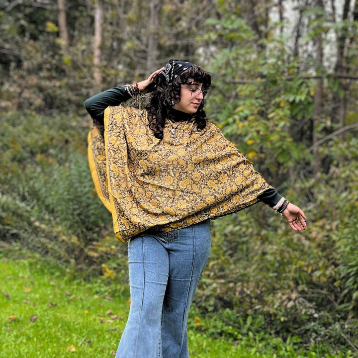 A woman wearing a poncho with trees in the background.