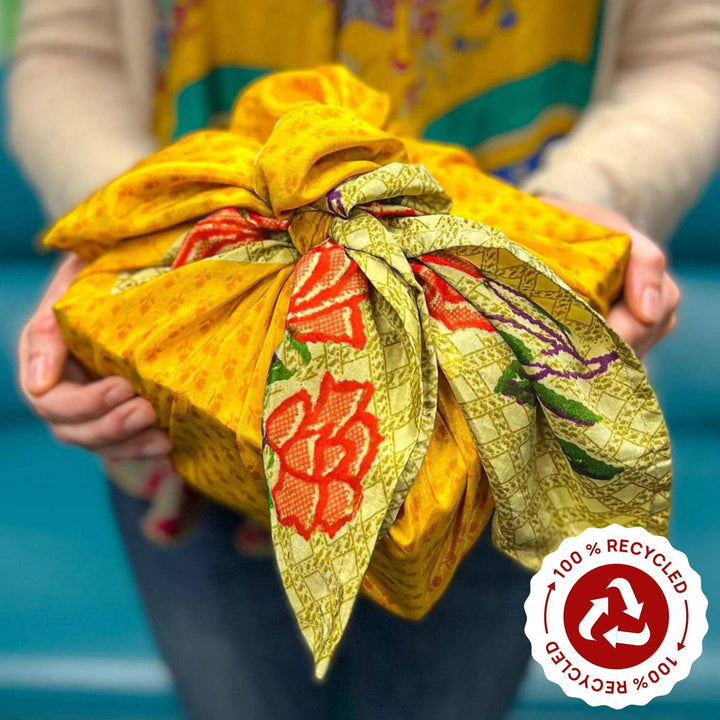 A girl wearing a sari silk medley scarf holding a present wrapped in a gold and orange furoshiki sari silk gift wrap.