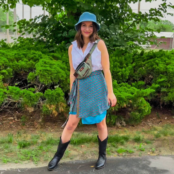 Model is wearing a blue womens mini sari wrap skirt while standing in front of some bushes. 