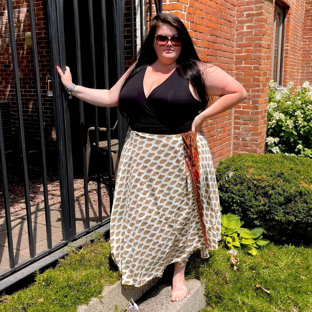 Model is standing outside by a garden gate wearing a white and tan maxi sari silk skirt.