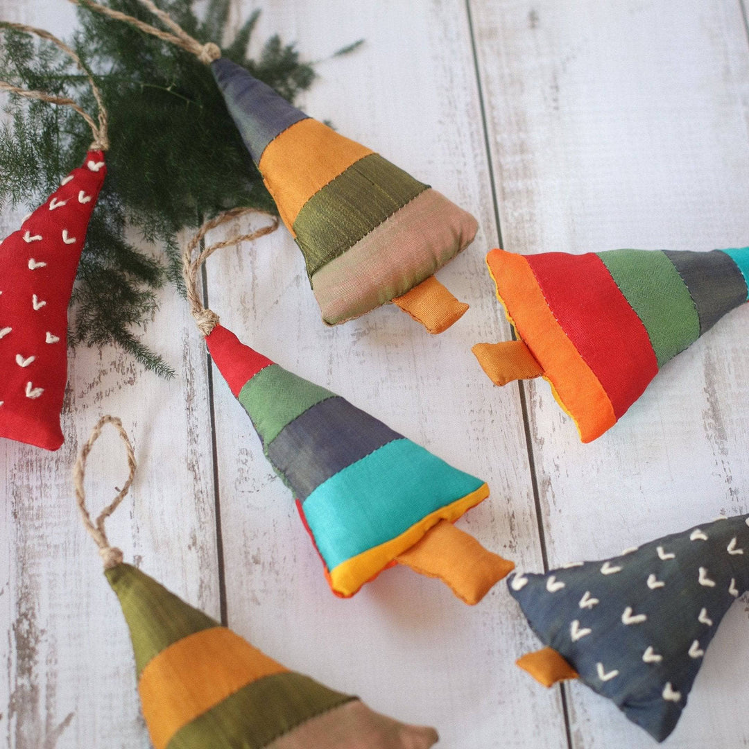 Small fabric Christmas tree shaped ornaments sitting on a tree branch with a white wood distressed background