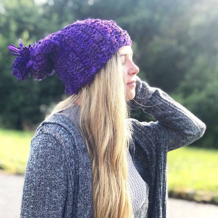 Side view of a girl wearing a purple sari ribbon hat outside with trees in the background