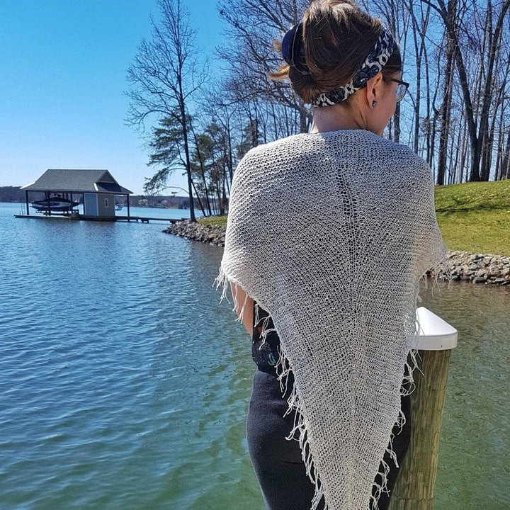 Back view of a woman wearing a white sarong outside standing next to a lake