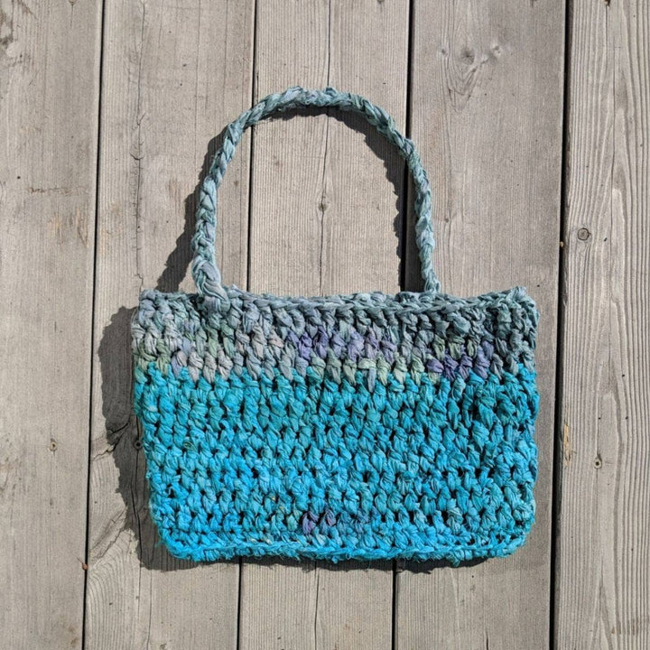 A blue and gray purse laying flat on a wooden background 