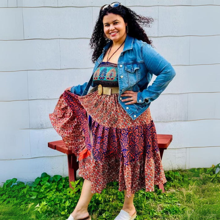 Woman in a colorful patchwork dress, smiling, paired with a denim jacket outdoors.