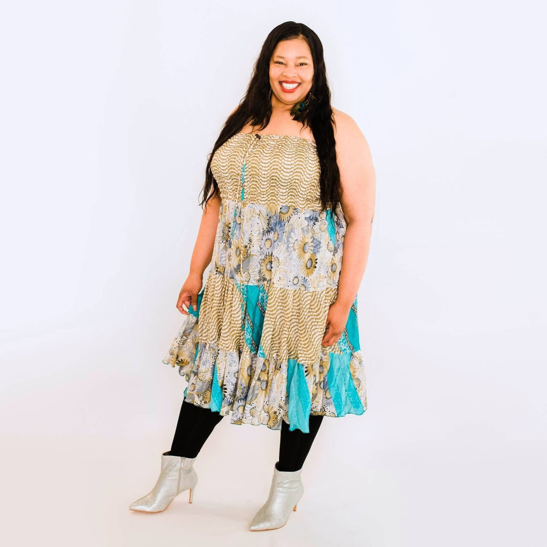 Woman in a multicolored dress and silver boots, smiling against a plain white background.