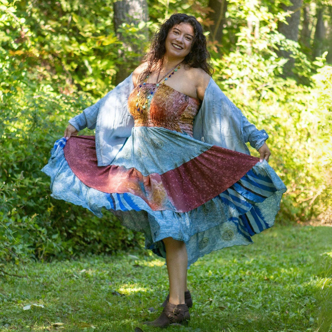 Smiling woman twirling in a colorful patchwork dress in a lush green