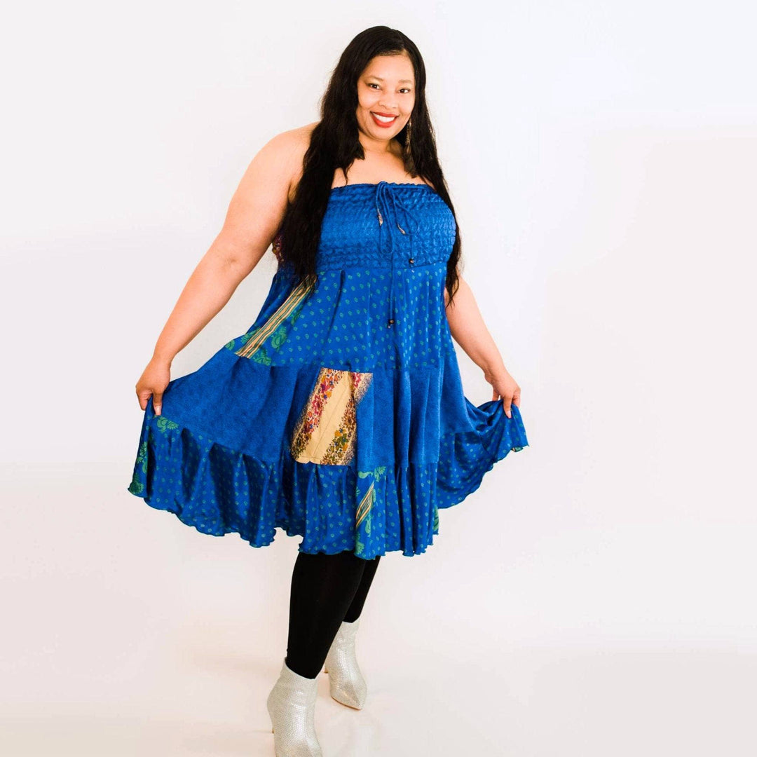 Person in a blue dress with colorful patches and white boots, smiling against a plain background.