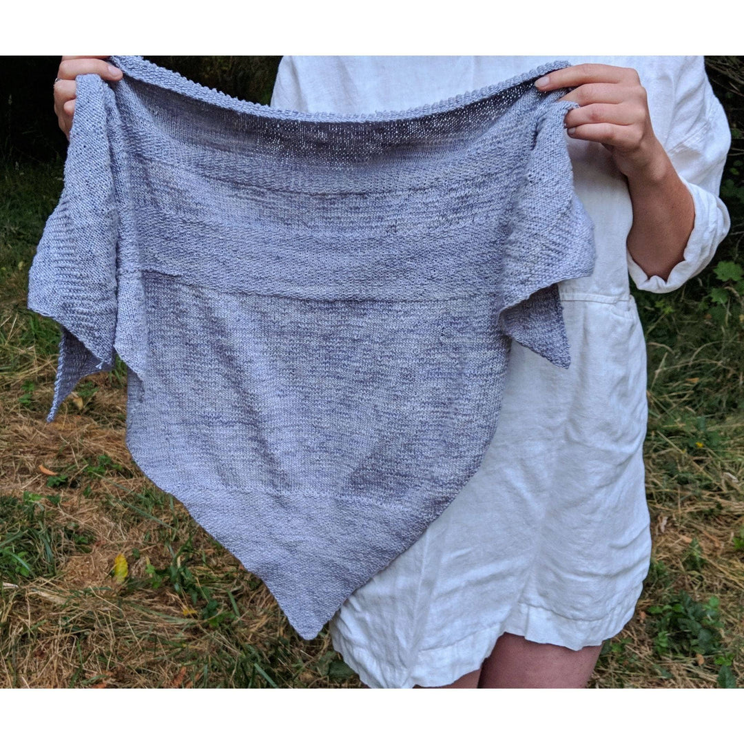 Designer holding up serendipity lace weight silk shawl with grassy background. 