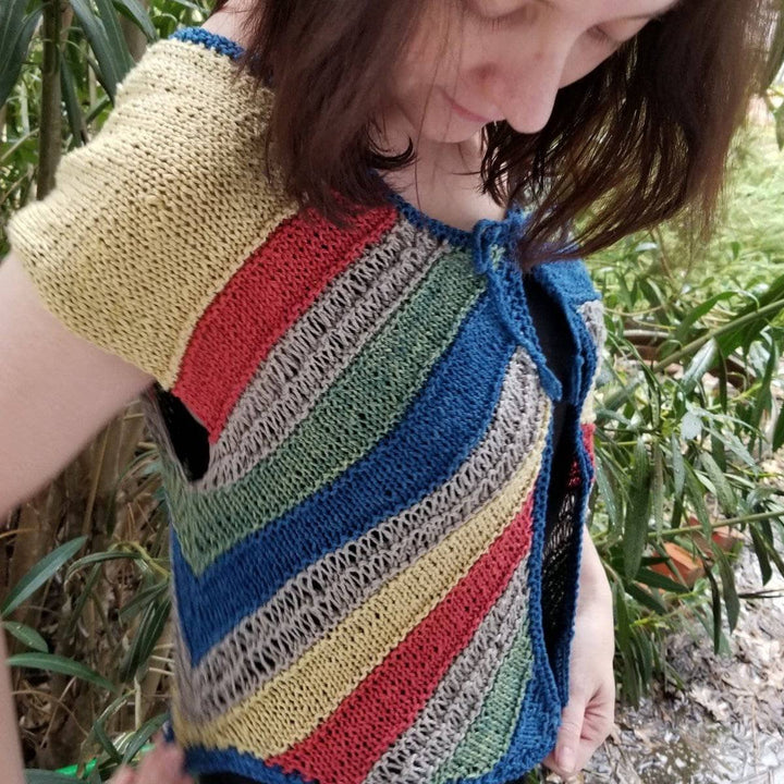 A side view of a women wearing a yellow, red, tan, green and blue stripped cardigan with trees in the background