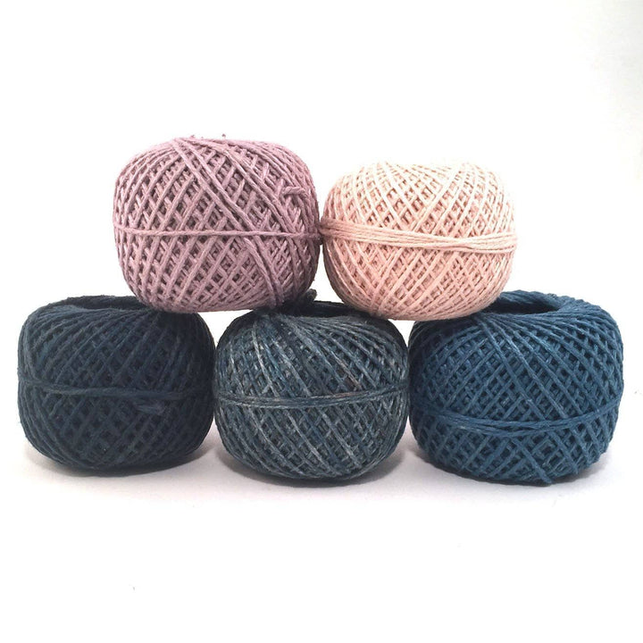 A dark pink, light pink, dark navy blue, light blue gray and medium blue cakes of yarn on a white background