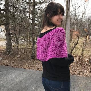 A side facing view of a woman wearing purple pink shawl wrap with trees in the background 