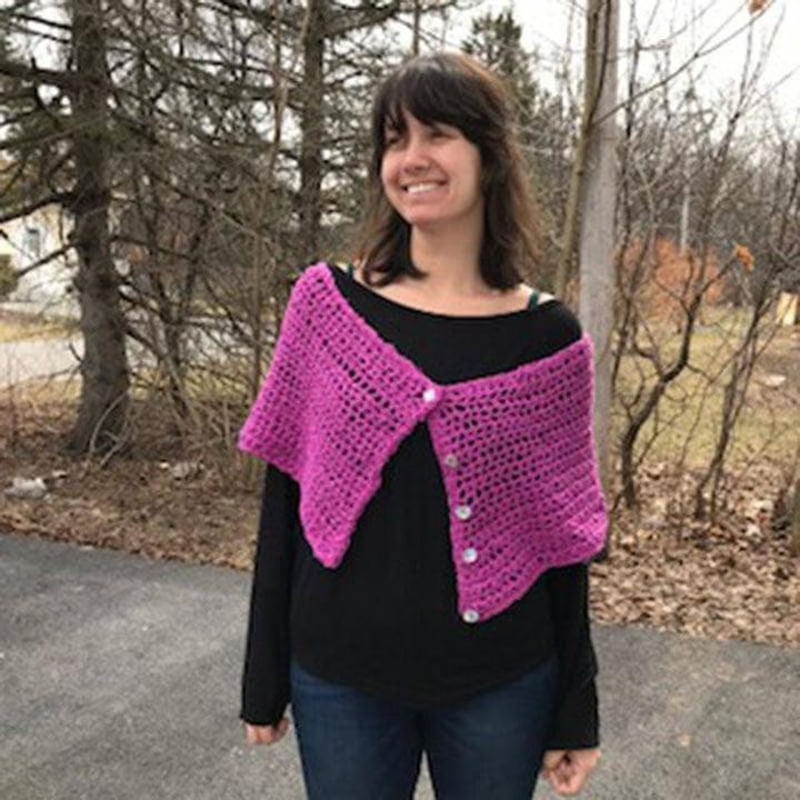 A front facing view of a woman wearing purple pink shawl wrap with trees in the background 