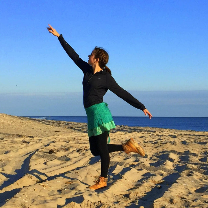 A junior model is wearing a green sari wrap skirt while on the beach. 