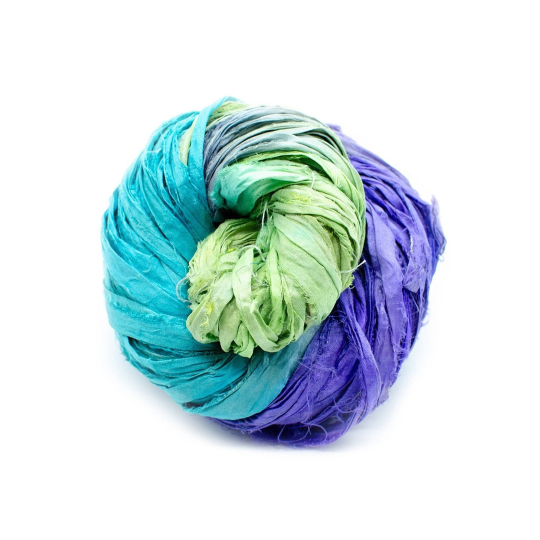 A ball of teal, green, and purple fabric strips, intertwined on a white background.