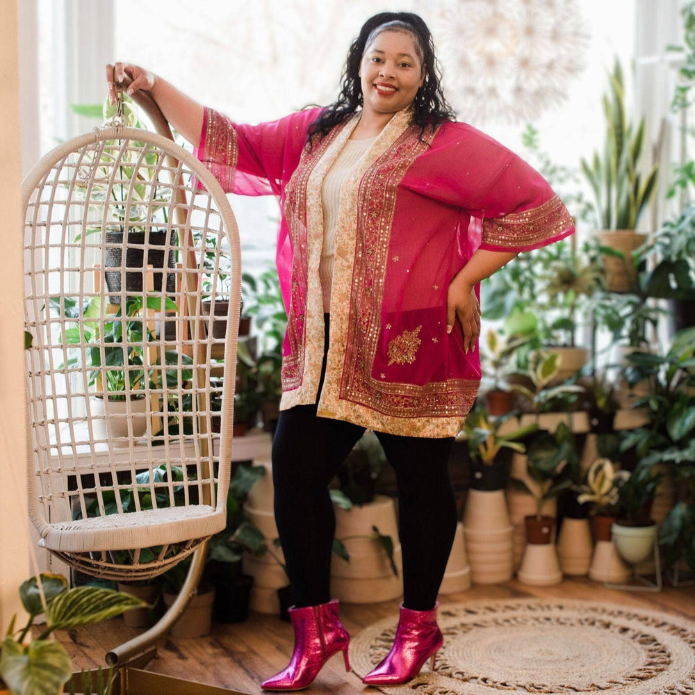 Person in a bright pink and gold jacket, black leggings, and pink boots holding a white chair.