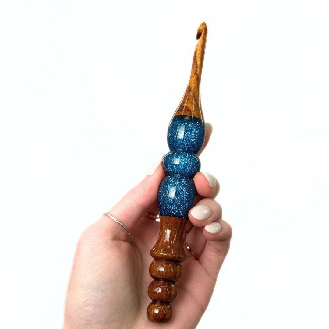 A woman's hand holing a  wooden and resin crochet hooks.