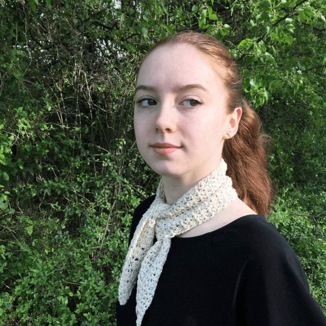 Woman wearing the Springtime City Mini Crochet Scarf in Cream in front of greenery 