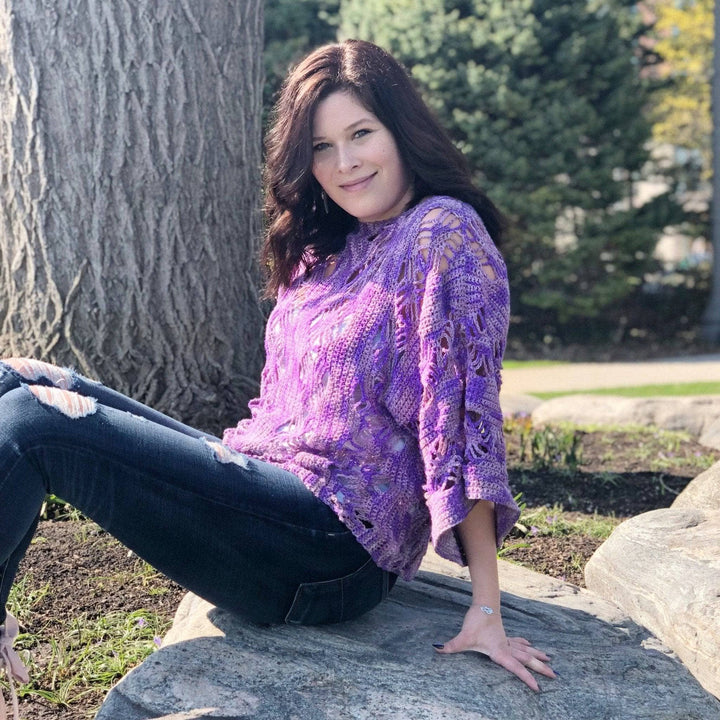 Woman wearing Stephanie's Web Tee while sitting on a rock in nature