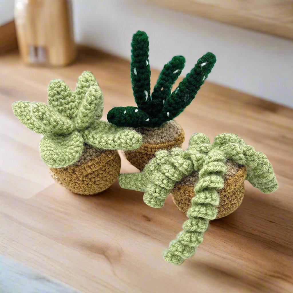 Three crocheted potted plants with green leaves and stems.