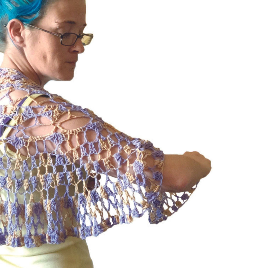 Model has the Summer's Breeze Shawlette drapped over their shoulders in front of a white backdrop. 