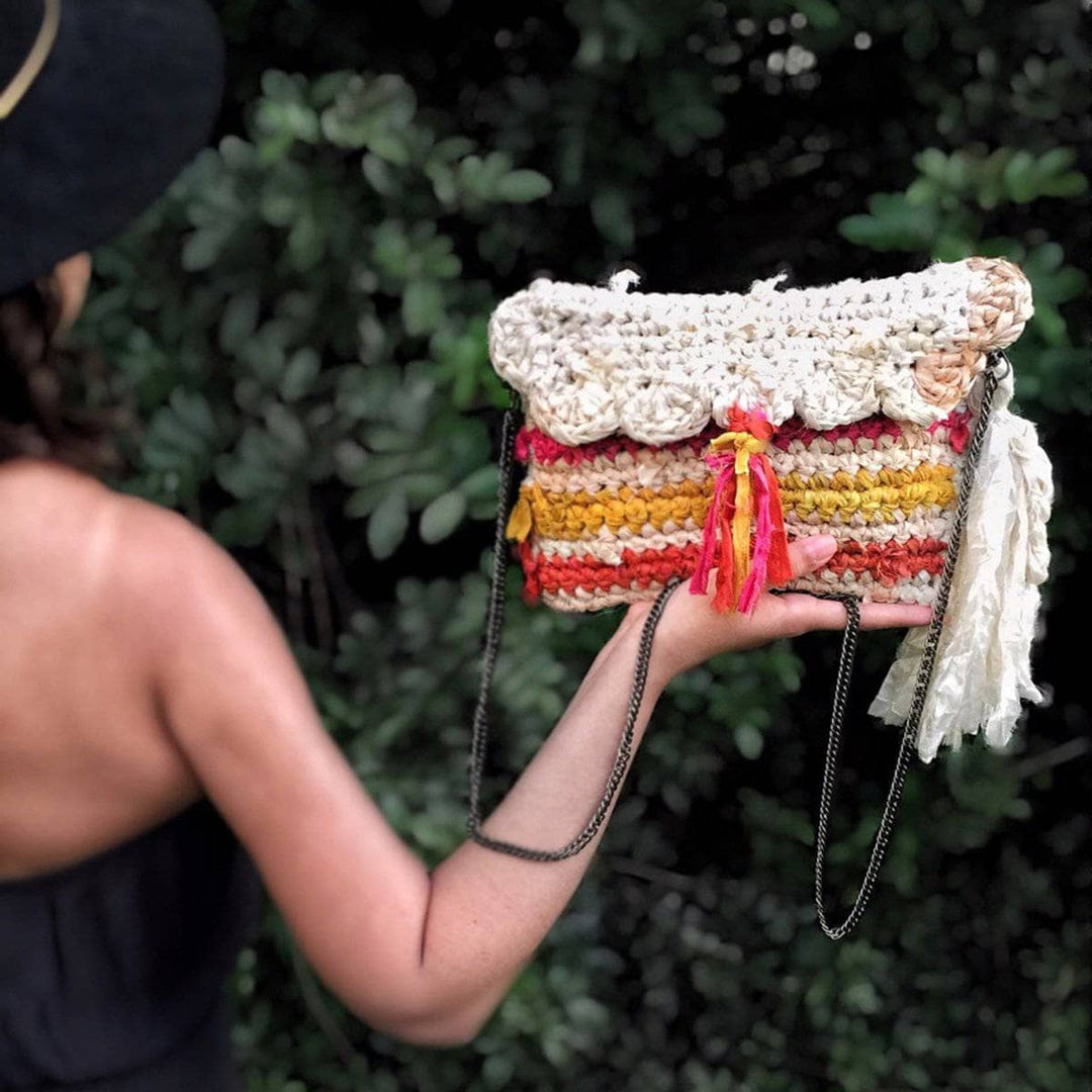 Woman's hand holding the Sun Burst Clutch in Sunset (cream, pink, orange) in front of greenery