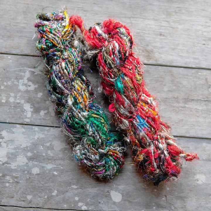 2 hanks of recycled silk yarn in the colorway indian festival laying parallel in front of a wood background.