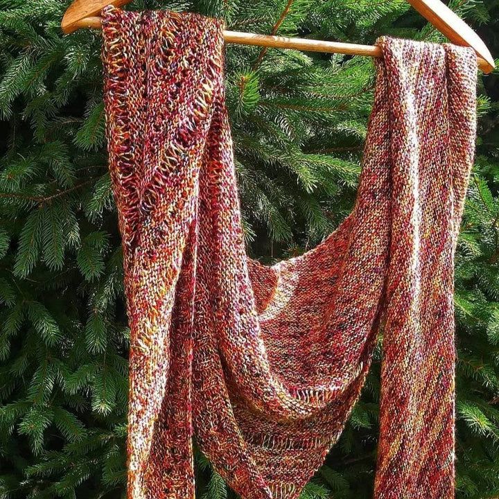 A specked red and yellow shawl hanging on a hanger on a tree