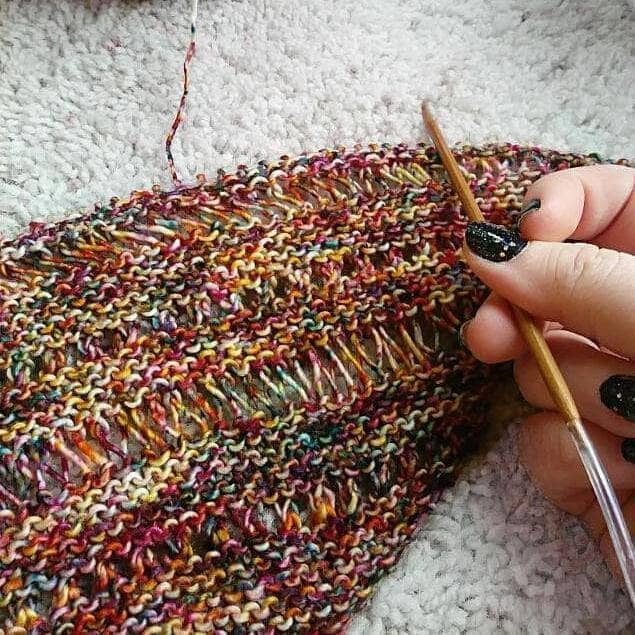 In progress picture of a red and yellow speckled shawl with a yarn bowl in the top of the picture on a white background