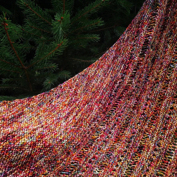 A specked red and yellow shawl hanging on a tree