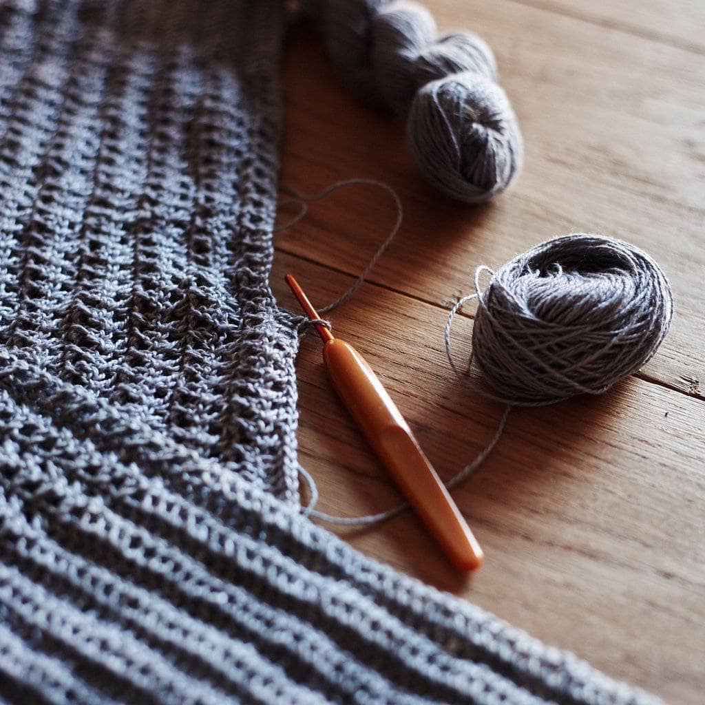 Partially made Crossed Stitched Top on a wooden surface with balls of yarn and a crochet hook