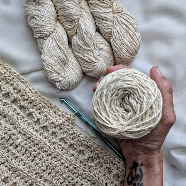 Close up of The Driftwood Tee Crochet Kit and partially made tee with woman's hands against a white background