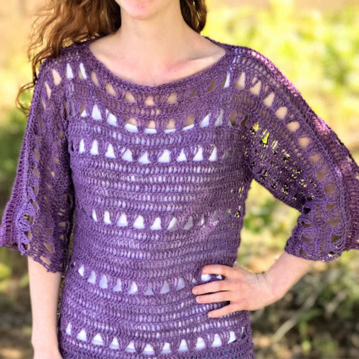 An up close shot of a woman standing outside wearing a Shelby Crochet Crop top made with purple 2-ply linen yarn.