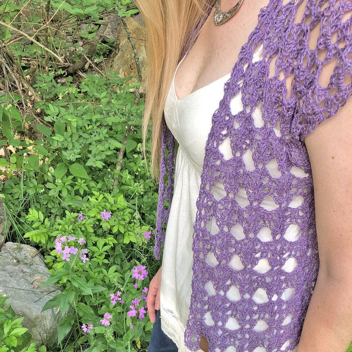 Woman wearing The Shenandoah Shrug in Purple standing in front of greenery