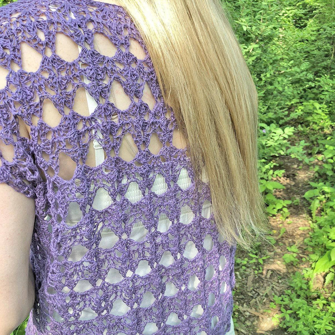 Woman wearing The Shenandoah Shrug in Purple standing in front of greenery