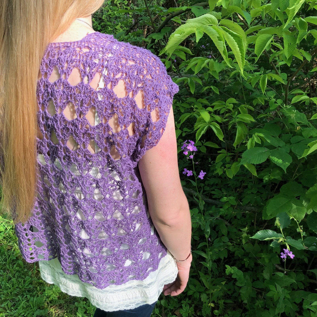 Woman wearing The Shenandoah Shrug in Purple standing in front of greenery