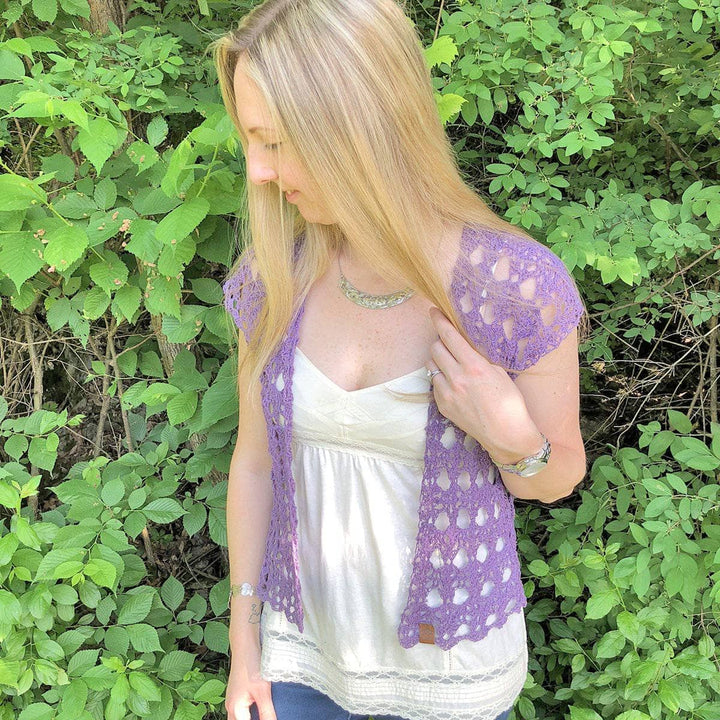 Woman wearing The Shenandoah Shrug in Purple standing in front of greenery