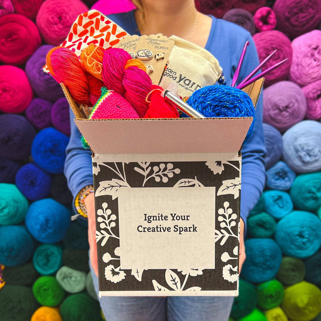 Woman holding an opened Mystery Black Box. Yarn, tools and notions spilling out. Yarn is made from recycled Silk.