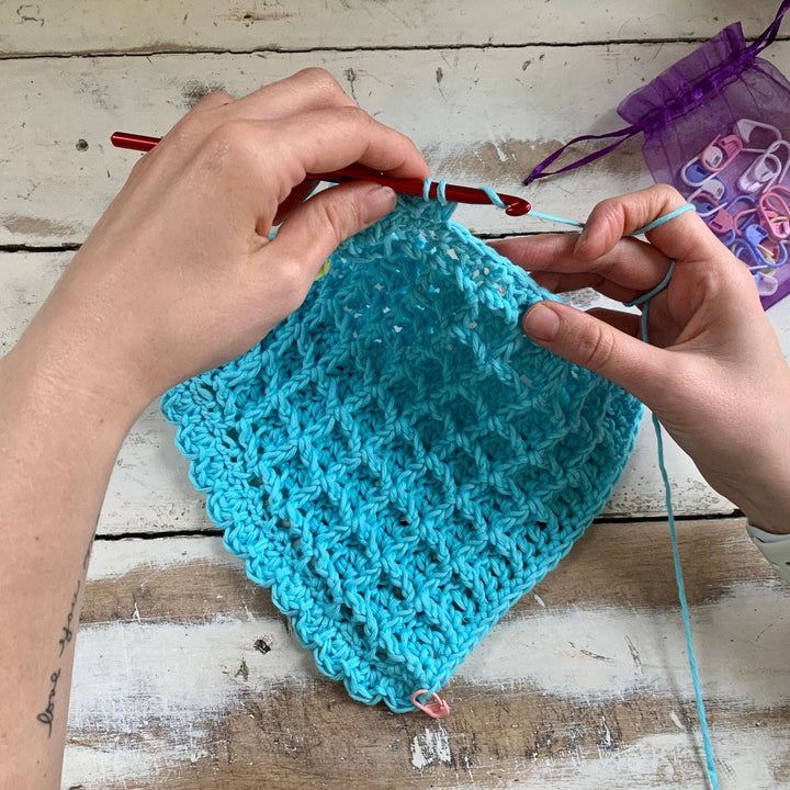 in progress photo of person crocheting a blue waffle stitch washcloth in front of a distressed wood background. 